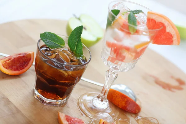 Two cocktails of whiskey with cola and grapefruit with ice vodka and mint. On a wooden board, fragments of fruit are flung up. Photo with depth of field. — Stock Photo, Image