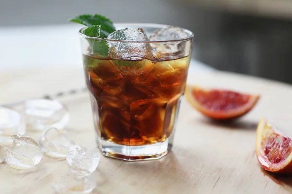 Cocktail cola med is i et glass. På treplanker finnes fruktfragmenter. Foto med feltdybde . – stockfoto