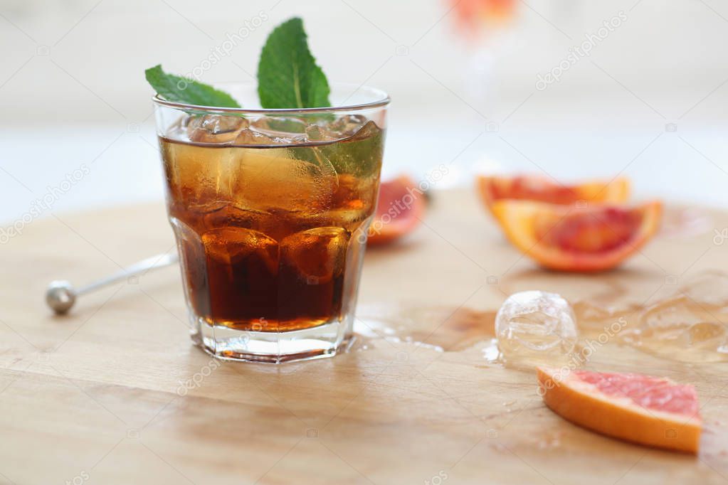 Cocktail whiskey cola with ice in a glass. On a wooden board are fragments of fruit. Photo with depth of field.