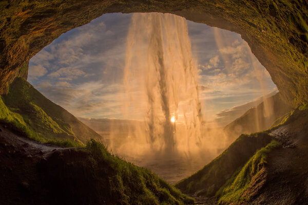 The waterfall Seljalandsfoss in the last golden light. One of the most famous waterfalls in Iceland. Shooted behind the waterfall at sunset. The sun's rays shine through the waterfall.
