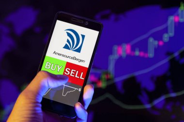 Yessentuki, Rusya - 27 Temmuz 2019: Akıllı telefon ekranında şirket logosu Amerisourcebergen Corporation (Abc.N), hisse senedi grafiğinin arka planında Buy or sell 'i gösteren bir tüccar eli