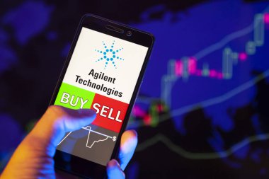 Yessentuki, Rusya - 27 Temmuz 2019: Akıllı telefon ekranında şirket logosu Agilent Technologies, hisse senedi grafiğinin arka planında Buy ya da sell 'i gösteren bir tüccar eli