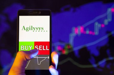 Yessentuki, Rusya - 27 Temmuz 2019: Şirket logosu Agilysys, Inc. (Agys) akıllı telefon ekranında, hisse senedi grafiğinin arka planında Buy ya da sell gösteren bir cep telefonu tutan tüccarın eli