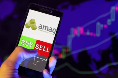 Yessentuki, Rusya - 27 Temmuz 2019: Akıllı telefon ekranında şirket logosu Amag Pharmaceuticals Inc, hisse senedi grafiğinin arka planında Buy ya da sell 'i gösteren bir tüccar eli
