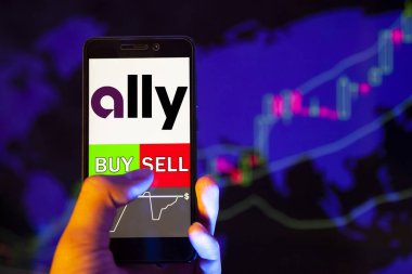YESSENTUKI, RUSSIA - July 27, 2019: Company logo Ally Financial Inc. on smartphone screen, hand of trader holding mobile phone showing BUY or SELL on background of stock chart clipart