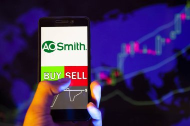 Yessentuki, Rusya - 25 Temmuz 2019: Şirket logosu A.O. Smith Şirketi akıllı telefon ekranında, elinde bir cep telefonu bulunan ve hisse senedi arkaplanında Buy ya da Satış 'ı gösteren bir el.
