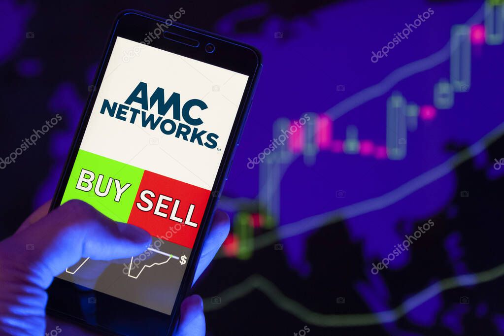 YESSENTUKI, RUSSIA - July 25, 2019: Company logo AMC NETWORKS Inc on smartphone screen, hand of trader holding mobile phone showing BUY or SELL on background of stock chart