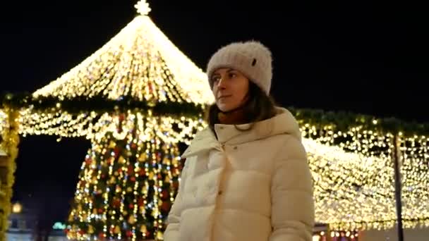 Mulher bonita em casaco e chapéu posando pela árvore de Natal na cidade — Vídeo de Stock