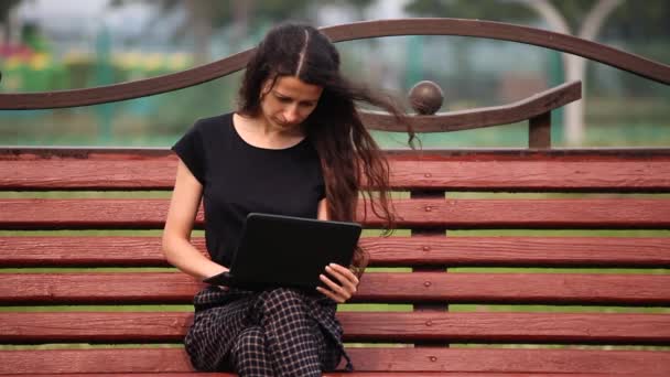 Mladá žena sedí na lavičce s prací na notebooku venku — Stock video