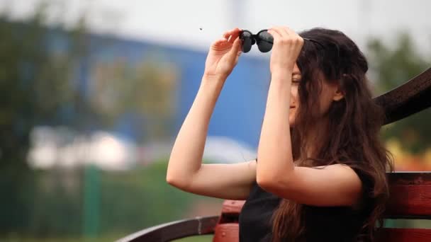 Portrait de jeune femme, elle dans le parc met des lunettes de soleil — Video