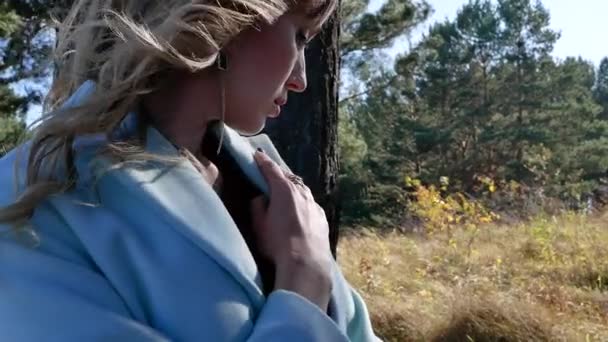 Портрет молодой сексуальной женщины с развивающимися волосами на ветру в пальто в осеннем лесу — стоковое видео