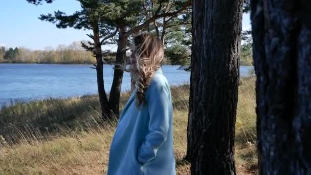 Jovem mulher loira bonita em um casaco azul assistindo lago na floresta de outono — Vídeo de Stock