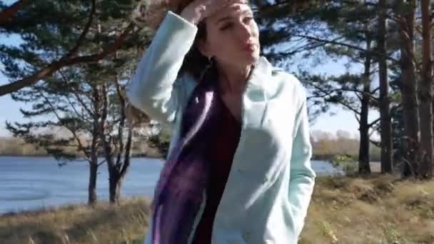 Beautiful young woman in blue coat walking down path in the autumn forest in windy weather — Stock Video