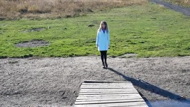 Young woman in blue coat goes over bridge on lake in autumn Sunny day — Stockvideo