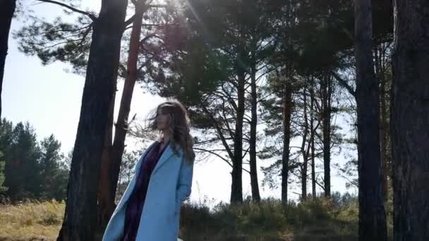 Beautiful young woman in blue coat standing in forest in windy weather autumn Sunny day — Stockvideo