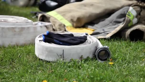 Wąż strażacki leżący na trawie z rękawiczką i kurtkami zbliżenie — Wideo stockowe