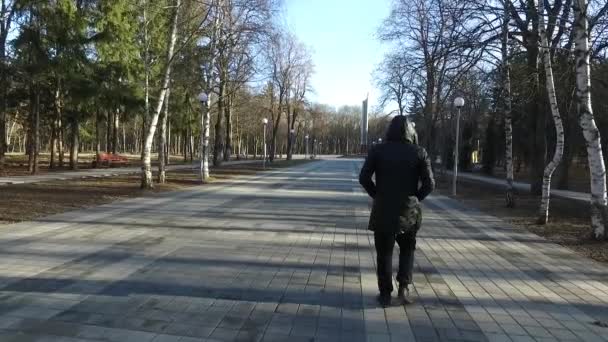 Nieznany mężczyzna w czarnym płaszczu z kapturem podąża ścieżką w jesiennym parku. Powoli. — Wideo stockowe