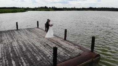 Aerial flight above of groom and bride hugging on wooden pier.  Camera moves in circle around
