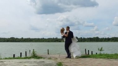 groom circling bride in his arms on pier at lake. copy space
