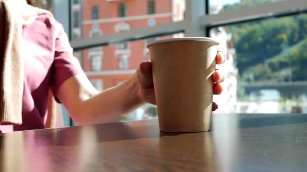 Jonge vrouw hand neemt papieren glas thee in cafe van tafel. thee drinken en glas op tafel zetten — Stockvideo