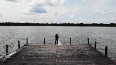Aerial flight above of groom and bride hugging on wooden pier, flying over lake