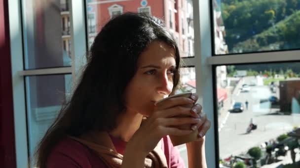 Fiatal nő a kávézóban az ablakban napos nyári nap iszik teát egy papír kupa — Stock videók