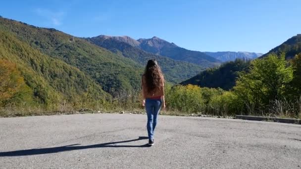 Hermosa joven se acerca acantilado en algún lugar de las montañas en verano al atardecer y extiende sus brazos hacia un lado. Concepto de libertad — Vídeos de Stock