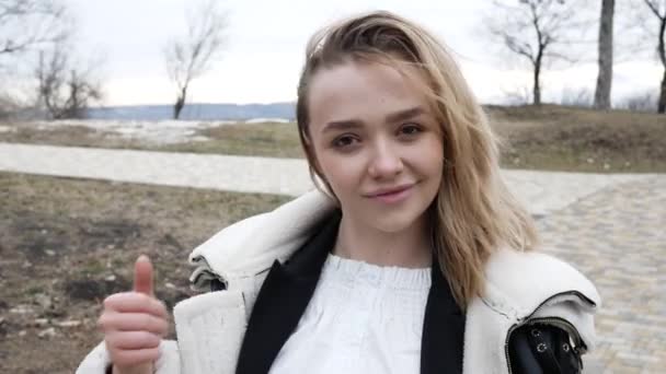 Portrait of young woman keeps thumb raised, being in good mood, shows her agreement, poses outdoors, says: Nice joke! Young woman shows like gesture, satisfied with something — Stock Video