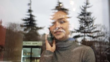 Kafede genç ve güzel bir kadın telefonda konuşuyor. Pencereden görünen.