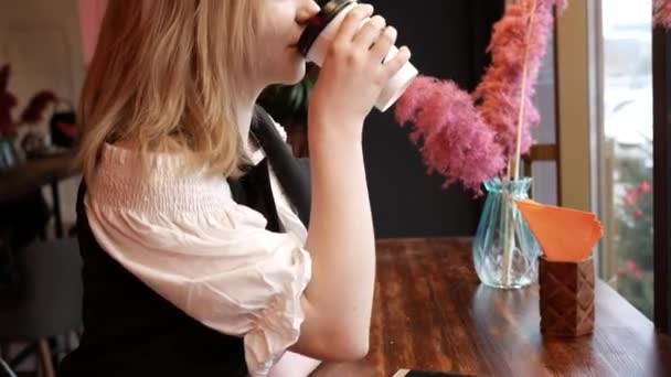 Hermosa rubia joven en la cafetería por ventana beber café de papel Copa — Vídeos de Stock
