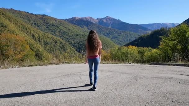 Hermosa joven se acerca acantilado en algún lugar de las montañas en verano al atardecer. Concepto de libertad — Vídeos de Stock