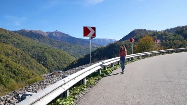 Молодая женщина, идущая летом по горной дороге на закате и наслаждающаяся видами гор — стоковое видео