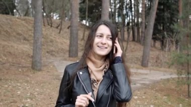 Deri ceket giyen, güz parkında yürüyen, cep telefonuyla konuşan güzel, genç ve neşeli bir kadın. Arayan kişiyi duyduğuna sevindi.