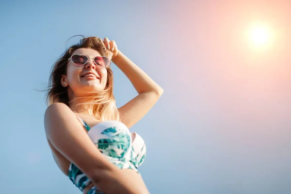 Mooie jonge vrouw in bikini en zonnebril op het strand bij zonsopgang — Stockfoto