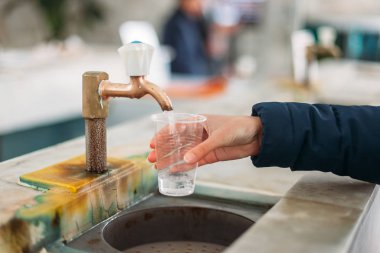 Drinking gallery of mineral spring. close - up of young woman gaining glass of mineral water from tap
