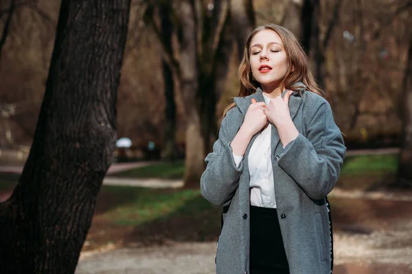 PA 에서 포즈를 취한 회색 코트를 입은 젊은 여성 사업가의 사진 — 스톡 사진
