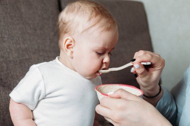 Genç anne kızını bir kaşık meyve püresiyle besliyor.