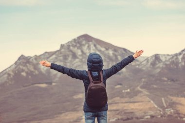 Arka plandaki dağlarda kollarını havaya kaldırmış bir adam. Arkadan görünüm