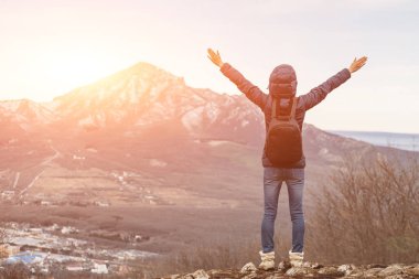 Dağlarda yürüyüş yapan, kollarını havaya kaldırmış biri. Arkadan görünüm