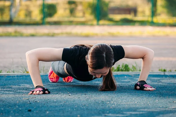 Belle brune mince faisant quelques push-ups à l'extérieur dans le parc. Ajustement — Photo