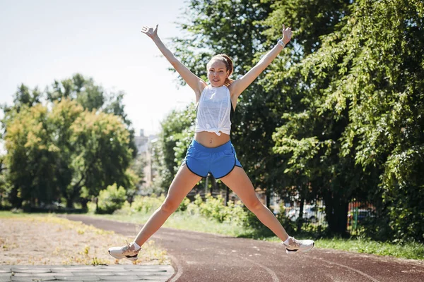 Happy sporty young woman jumps in height at sports stadium, rejo — Φωτογραφία Αρχείου