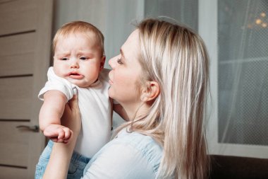 Evde, annemin kollarında ağlayan bir bebek, annem teselli ediyor.