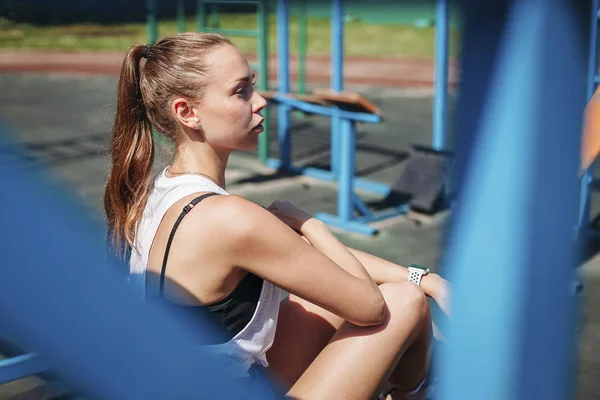 Atlético jovem loira mulher senta-se e descansa no campo desportivo durante — Fotografia de Stock