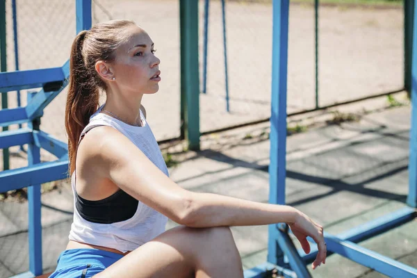 Спортивная молодая блондинка сидит и отдыхает на спортивной площадке во время — стоковое фото