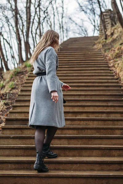 Молода дівчина в сірому пальто піднімається сходами в парку восени — стокове фото