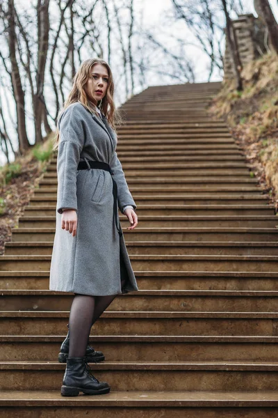Una giovane ragazza in cappotto grigio scende le scale nel parco in autunno — Foto Stock