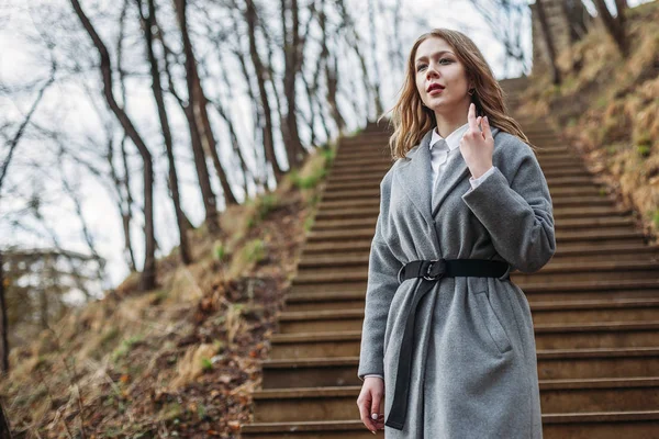 Beautiful young blonde woman in gray coat posing on stairs in pa — Stock Photo, Image