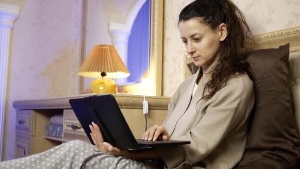 Jovem trabalha no quarto na cama em um laptop — Vídeo de Stock