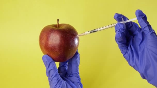 リンゴへの注射だ。黄色の背景に注射器で医療用手袋を手。遺伝子組み換え食品。ガスの注入. — ストック動画