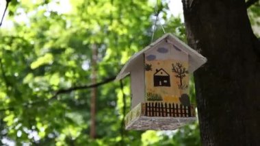 Yaz bahçesindeki bir ağaçta asılı süslemeli kuş evi.